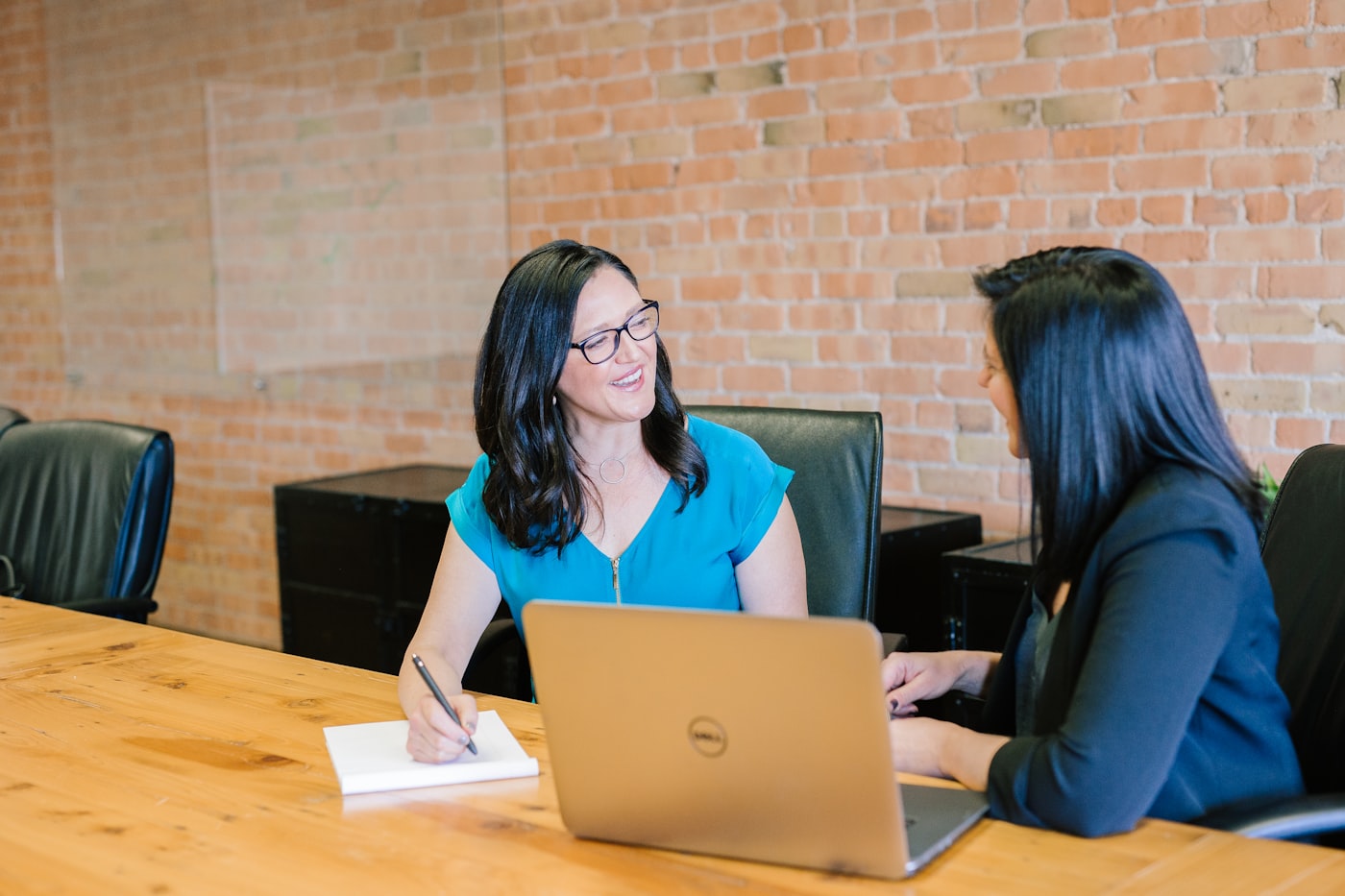 Two women in conversation at a desk in warm window light